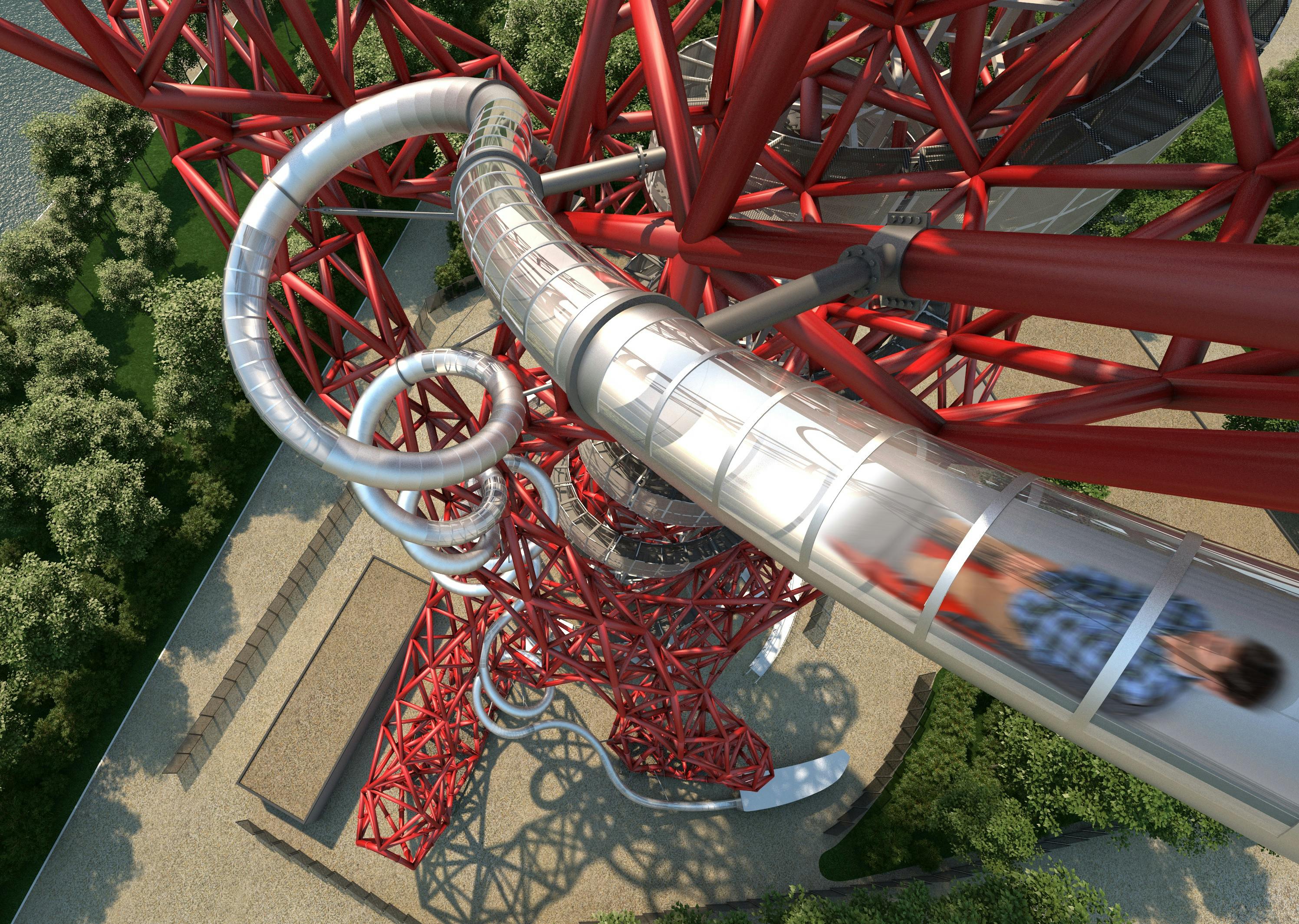 A person slides down an enclosed twisting slide that wraps around a large red metal structure, surrounded by trees and pathways.