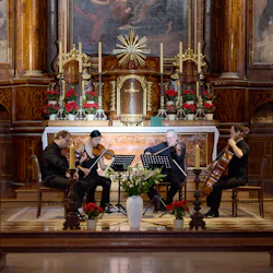 En stråkkvartett uppträder i ett dekorerat kyrkaltare, med deltagare som sitter i träbänkar och tittar på.