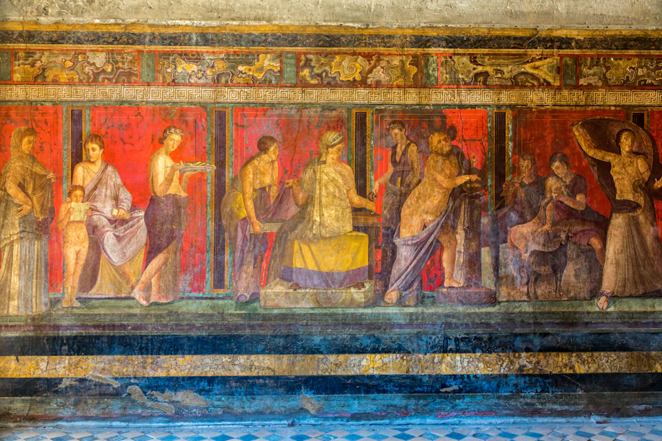 Ancient fresco depicting several figures in classical attire, engaging in various activities, on a red and gold background with intricate borders.