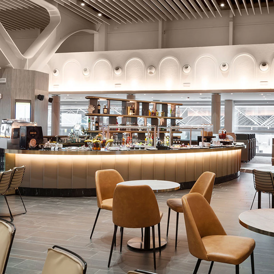 Modern cafe with a curved bar counter, well-lit shelves, tan chairs, and high ceilings with architectural details.