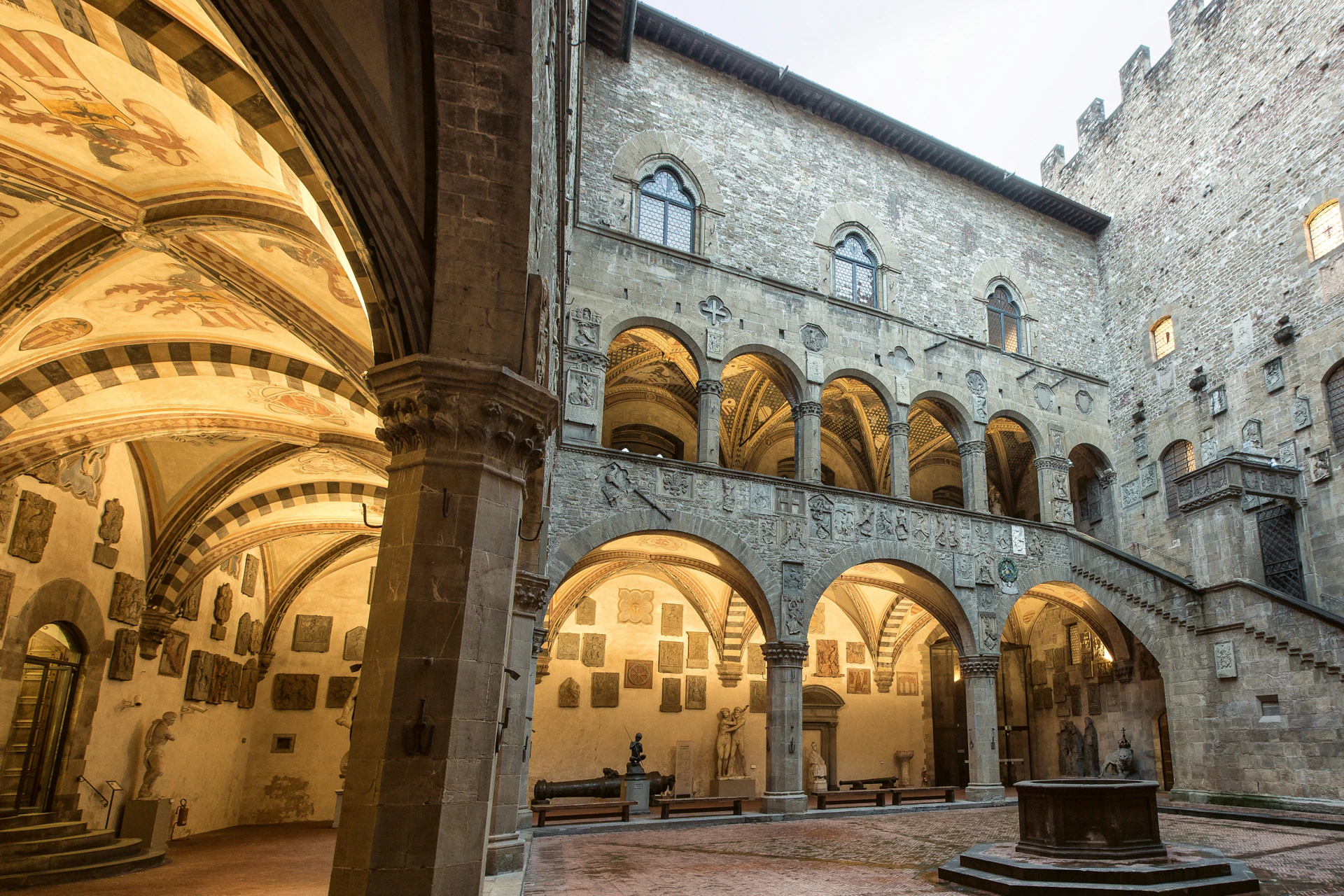 Historic courtyard with stone arches and decorative carvings, surrounded by a multi-story building with arched windows.
