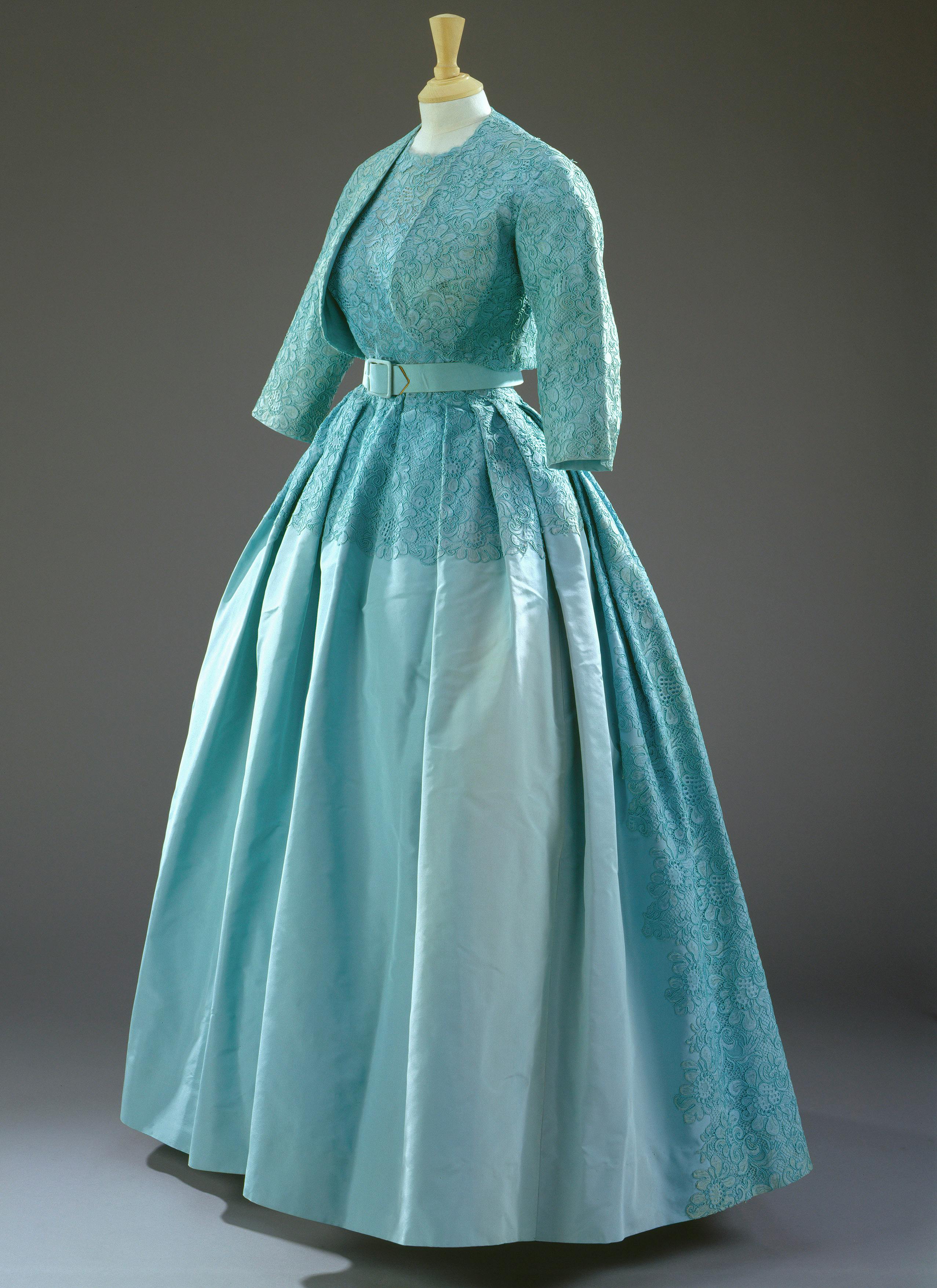 Ένα γαλάζιο vintage φόρεμα με εφαρμοστό μπούστο, μακριά μανίκια και μια πλήρη πλισέ φούστα που εμφανίζεται σε μια κούκλα μανεκέν.