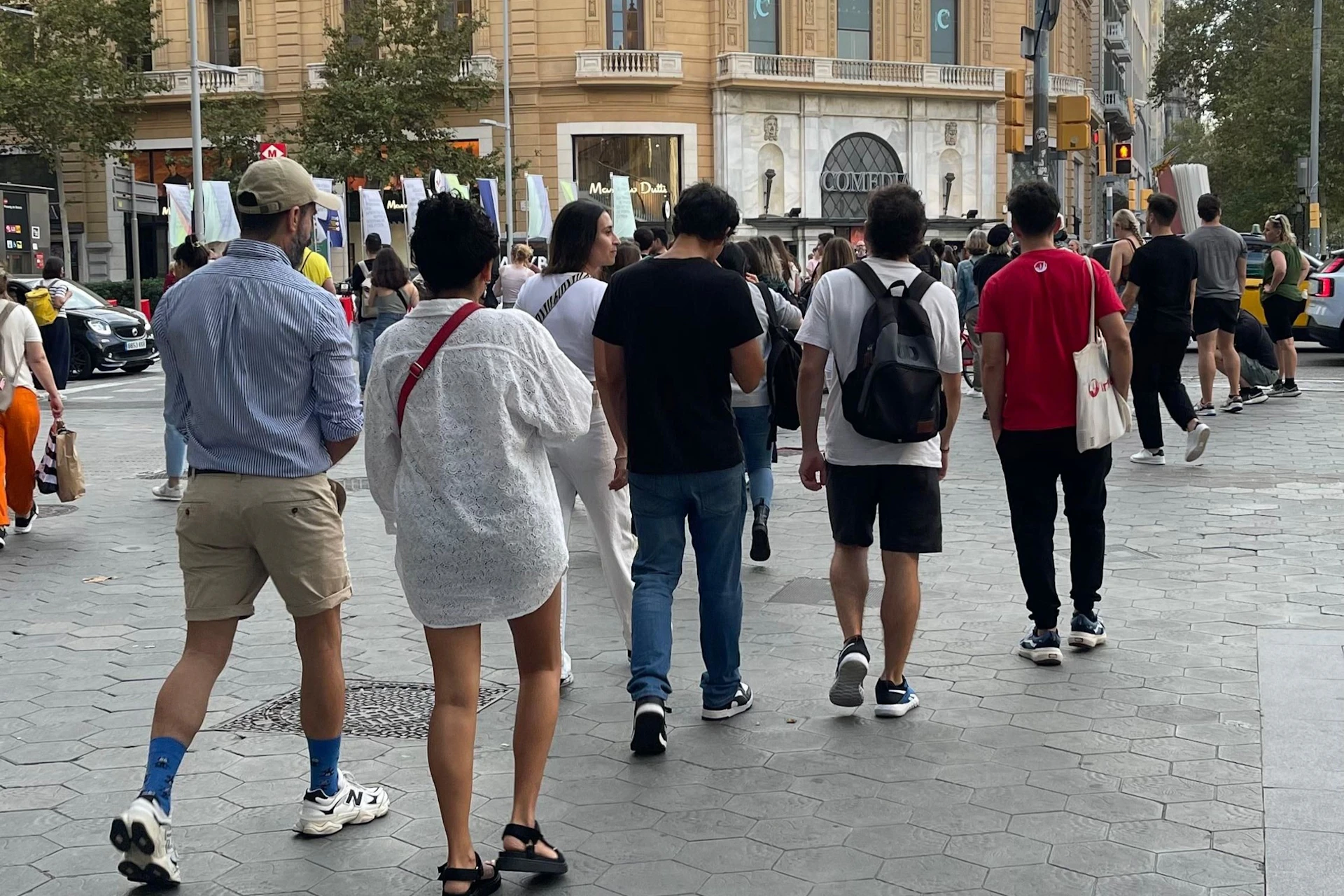 People walking on a busy street near a historic building with arched windows and columns.
