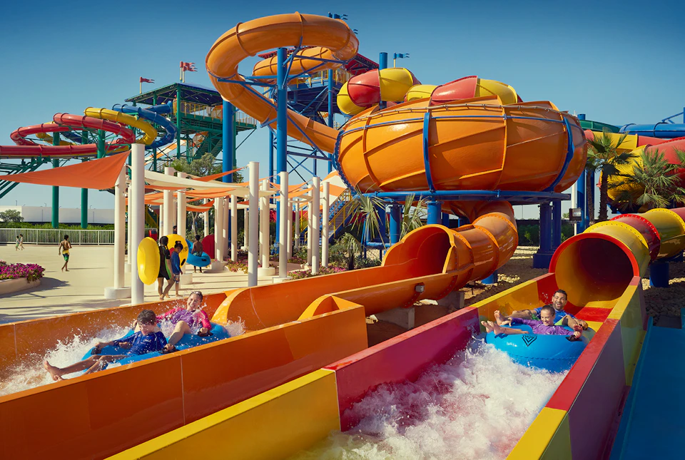 Children riding colorful water slides and floating in tubes at a vibrant water park on a bright day.