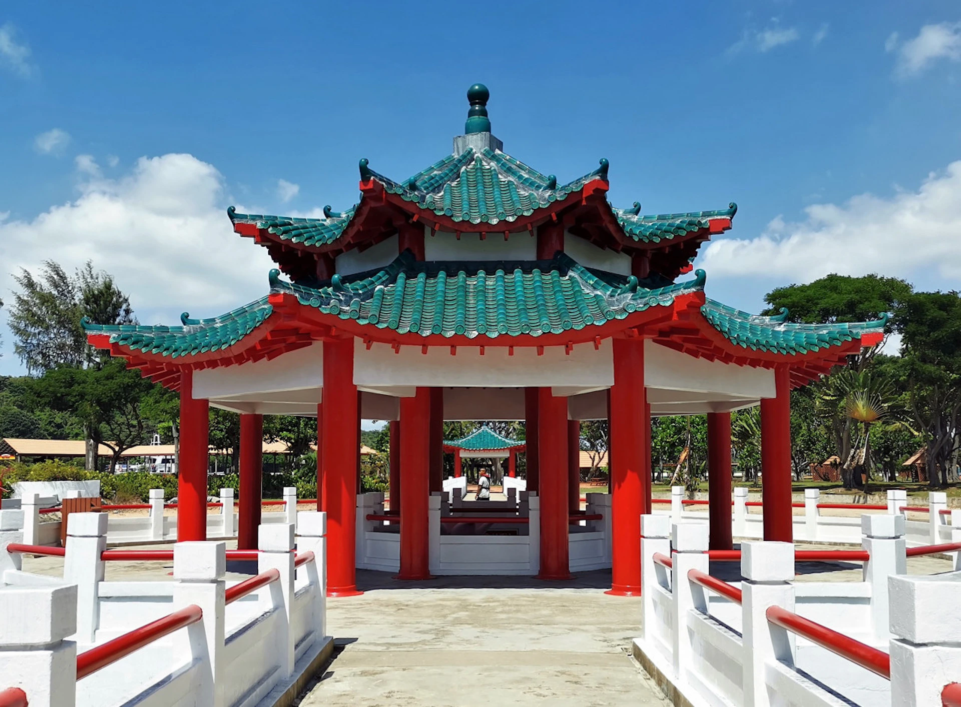 A traditional Chinese pavilion with green-tiled roofs and red pillars, set against a clear blue sky.