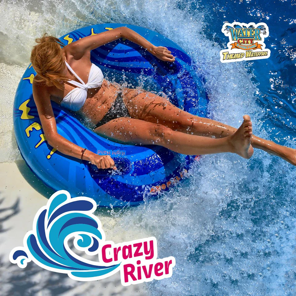 A person in a white bikini top rides a blue inflatable tube down a water slide. The text reads "Crazy River" and "Water City."