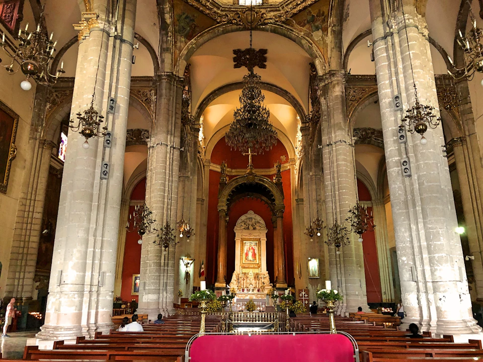 Interior of a ornate cathedral with tall columns, chandeliers, and an altar featuring religious artwork and decorations.