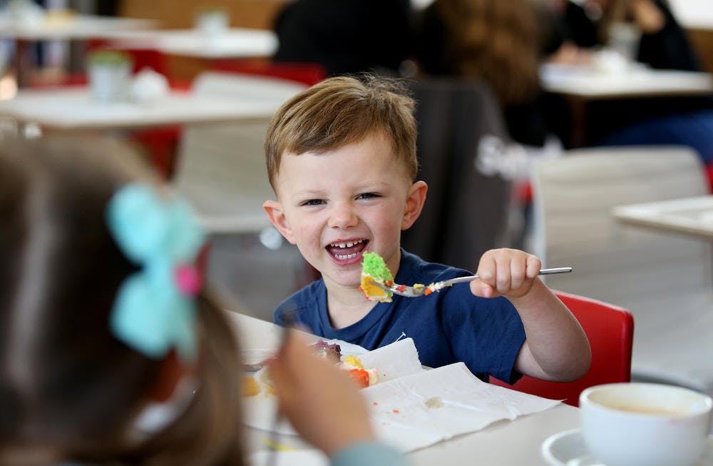 푸른색 셔츠를 입은 어린 아이가 캐주얼한 분위기에서 화려한 케이크를 먹으며 미소를 짓고 있습니다.
