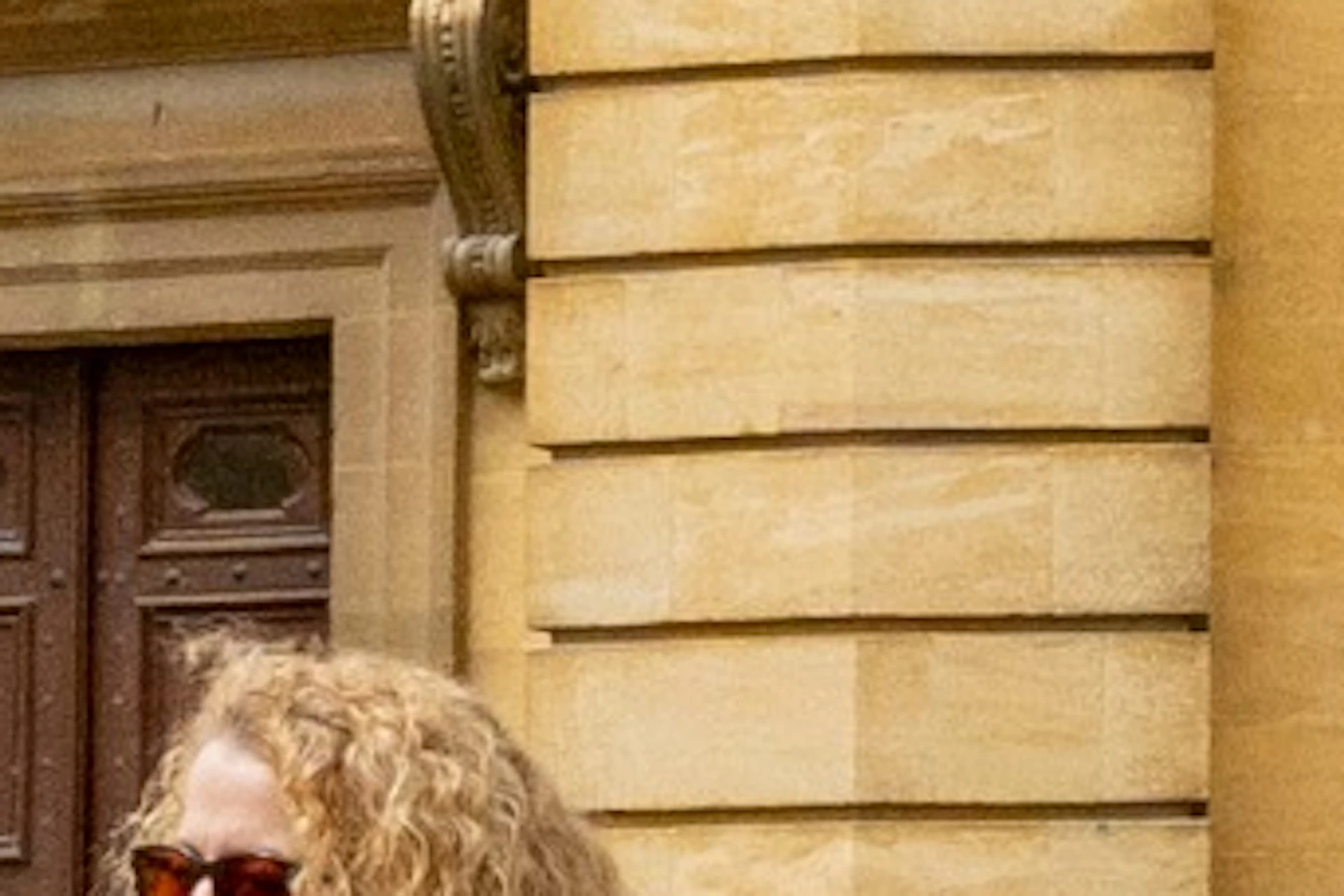A group of people on a guided tour in front of a historic yellow stone building with arched windows and a dome.