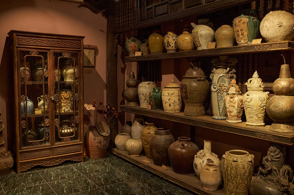 Shelves filled with antique pottery and a wooden cabinet displaying decorative items in a warmly lit room.