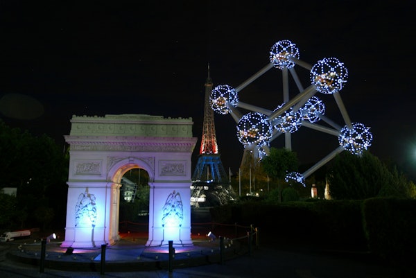Rèpliques il·luminades de l'Arc de Triomf, la Torre Eiffel i l'Atomium a la nit, situades contra un cel fosc.