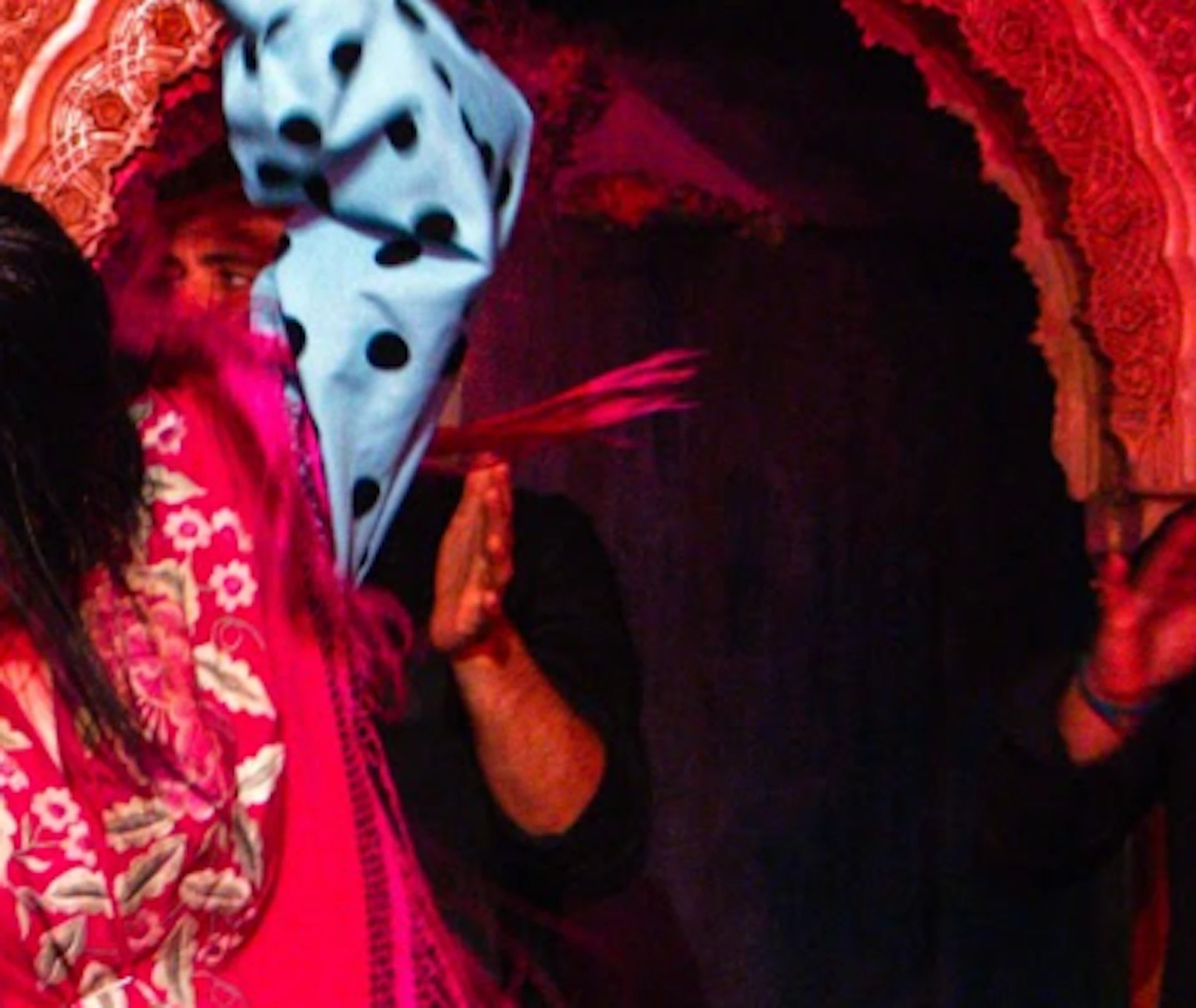 A flamenco dancer in vibrant attire performs energetically on stage, accompanied by musicians under red lighting.