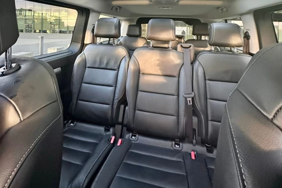 Interior of a vehicle showcasing three rows of black leather seats with headrests and seatbelts.