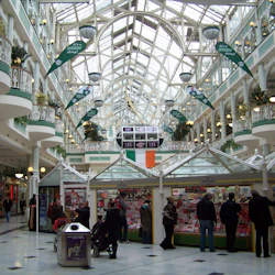 Ett köpcentrum inomhus med högt glastak, flera balkonger med växter och folk som surfar i en kortkiosk.
