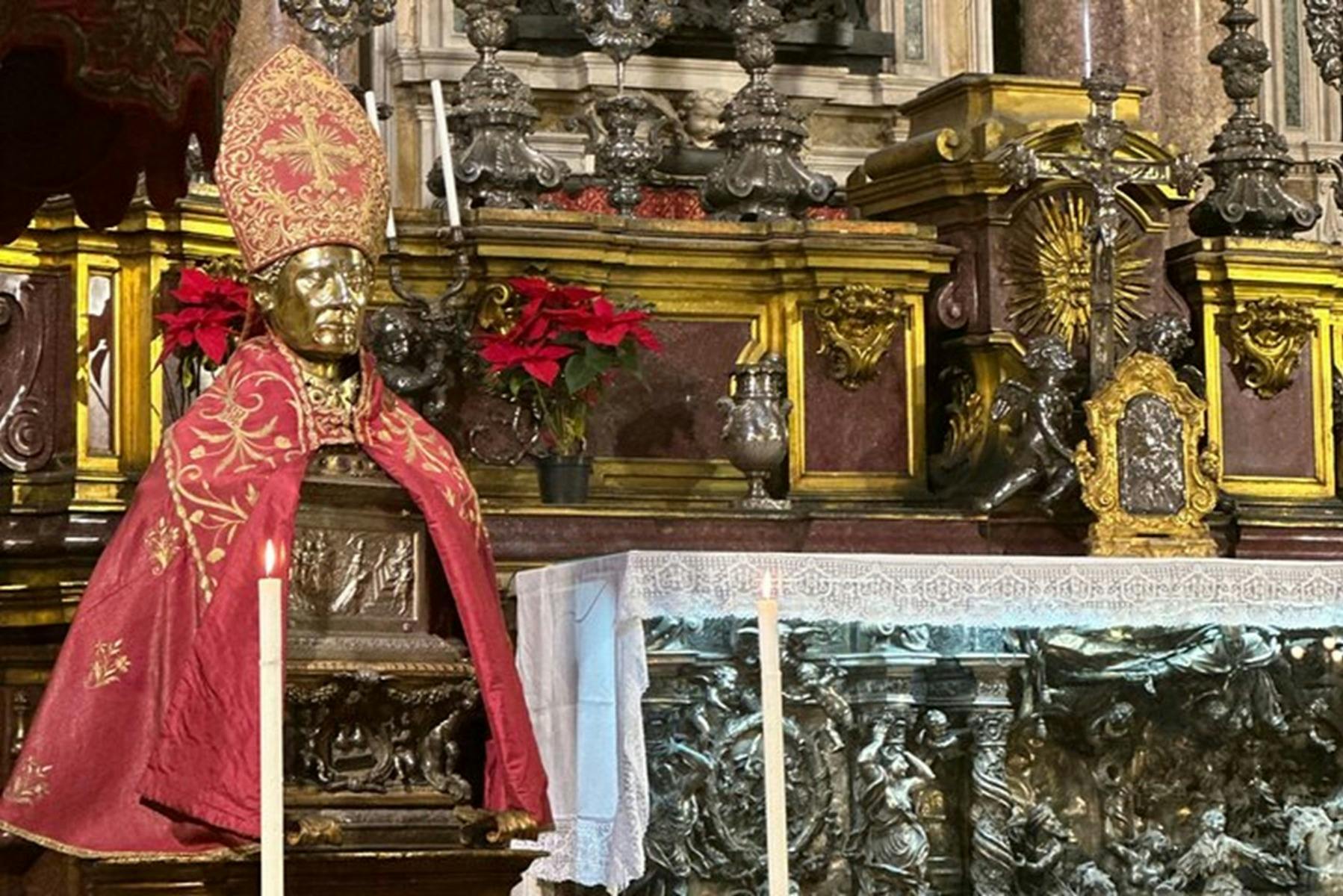 Una estàtua daurada amb un vestit vermell cerimonial en un altar decorat amb candelabros, poinsettias i talles intrincades.
