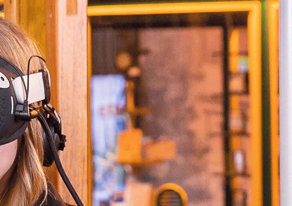 Two people wearing VR headsets, seated on a wooden bench indoors, appear to be immersed in a virtual reality experience.