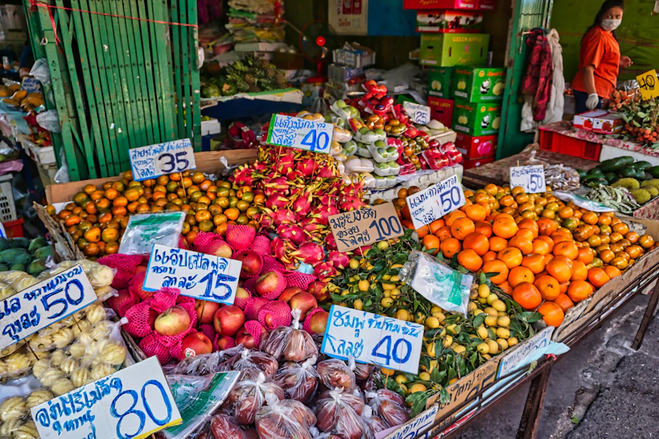 A market stall displaying various fruits and vegetables with handwritten price signs in a colorful arrangement.