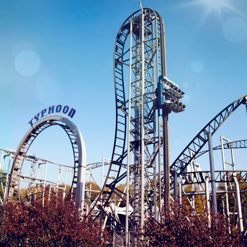 En berg- och dalbana med namnet "Typhoon" med flera slingor och vridningar under en klarblå himmel, omgiven av träd och buskar.