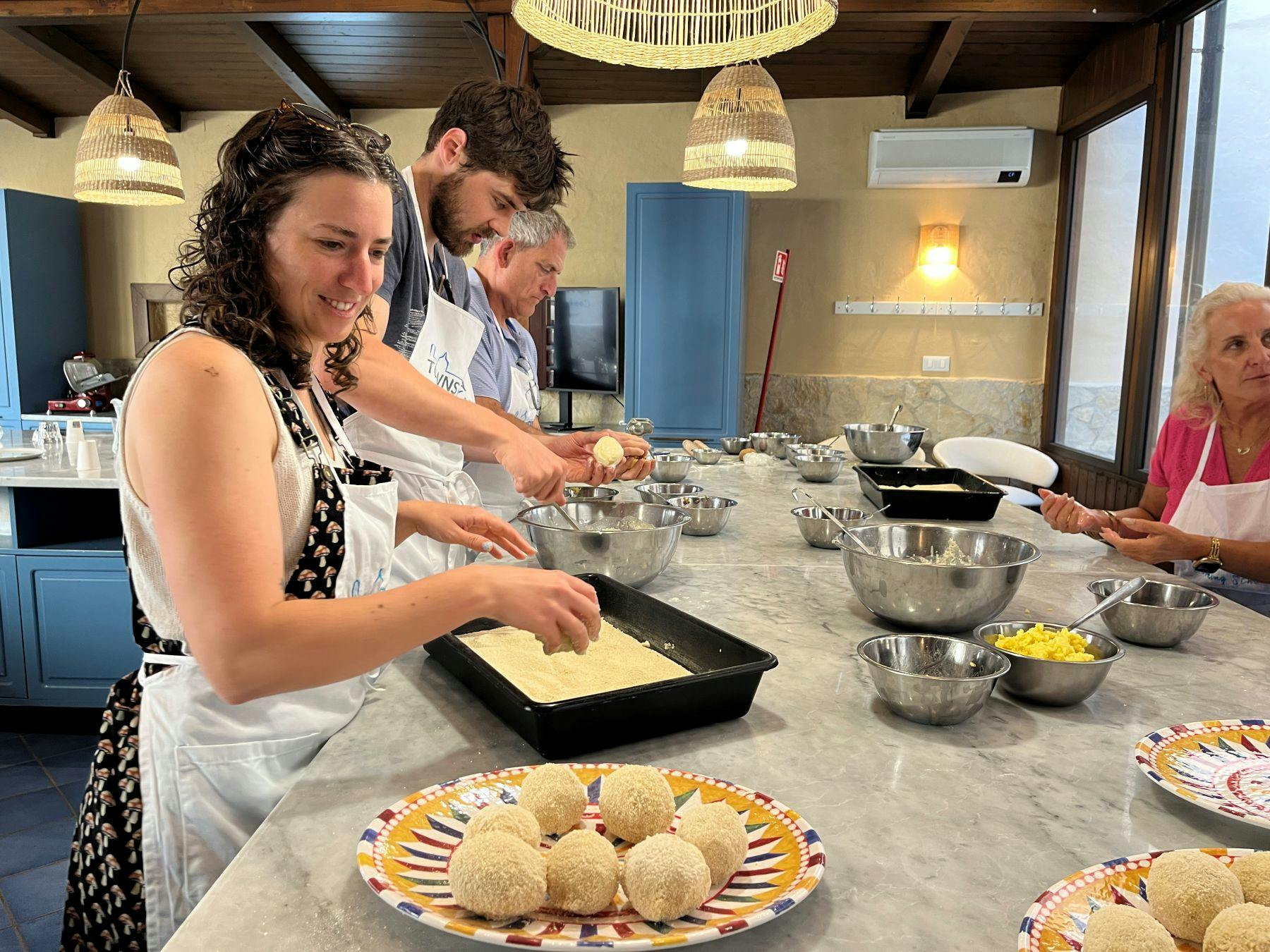 Three people in aprons preparing breaded food items at a kitchen counter, with bowls and plates on the surface.