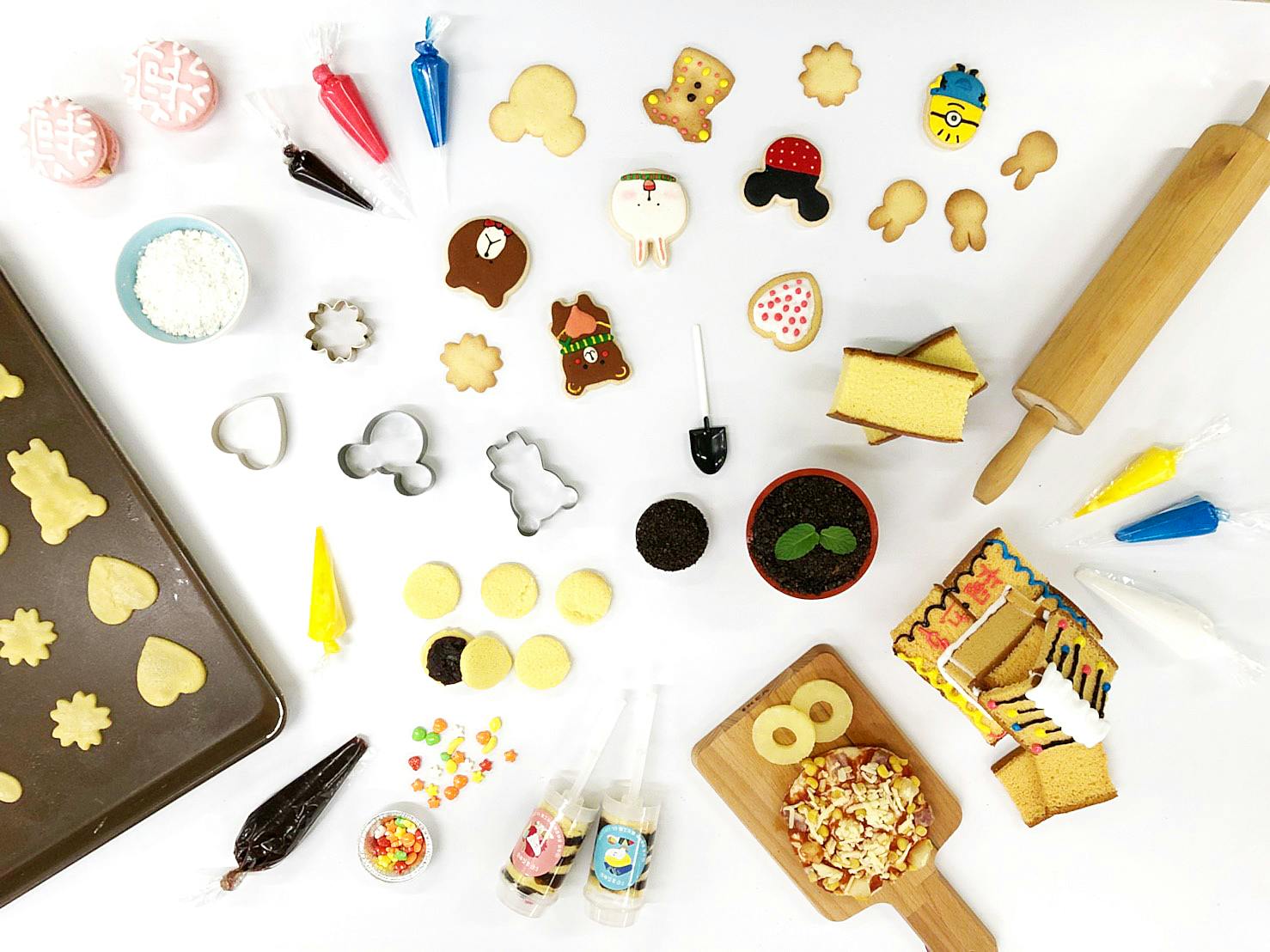 A collection of decorated cookies, baking tools, and ingredients arranged on a white surface in a flat lay style.