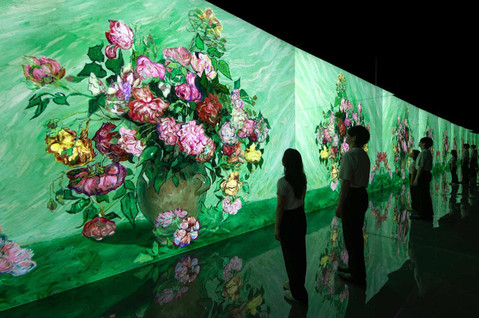 Two people viewing a digital art display of colorful floral arrangements on curved walls with a green background.