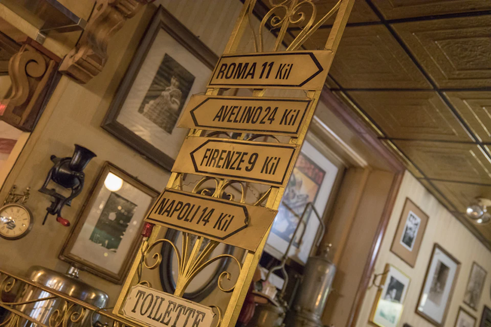 Vintage directional signs for Roma, Avelino, Firenze, Napoli, and Toilette in an eclectic interior with framed pictures.
