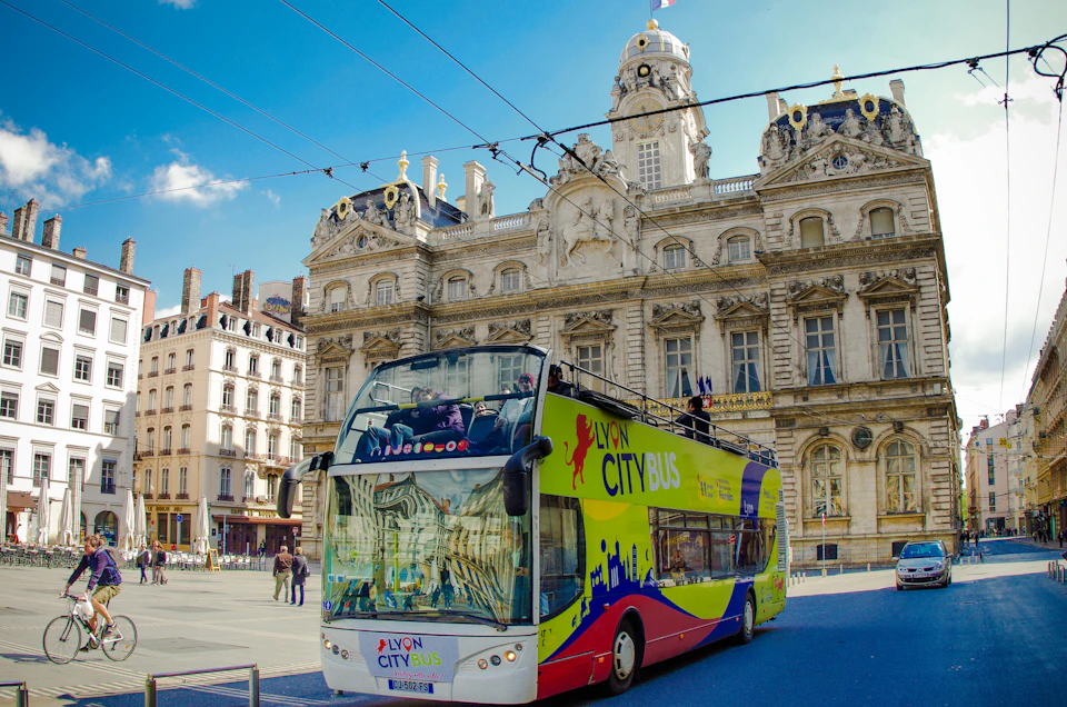 A colorful double-decker Lyon City Bus in front of an ornate historic building under a clear blue sky.