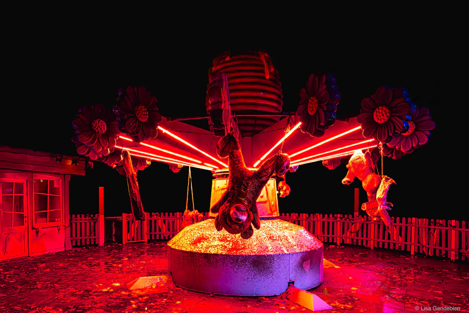 A carousel-like structure with suspended animal figures, lit dramatically with red light, against a dark background.
