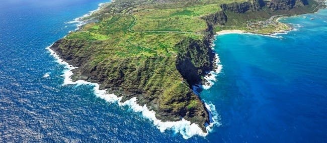 Vista aèria d'un paisatge costaner accidentat amb penya-segats, vegetació verda i onades blaves al llarg de la riba.