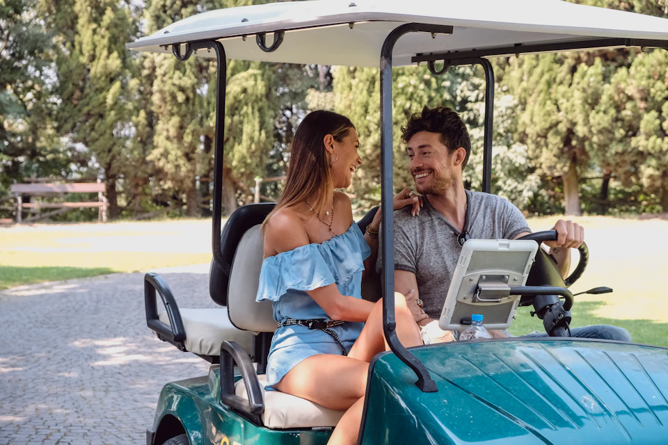 A couple smiling at each other while sitting in a golf cart with trees in the background.