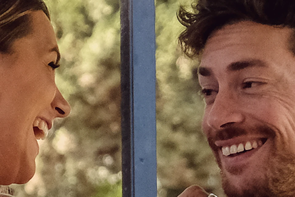 A couple smiling at each other while sitting in a golf cart with trees in the background.