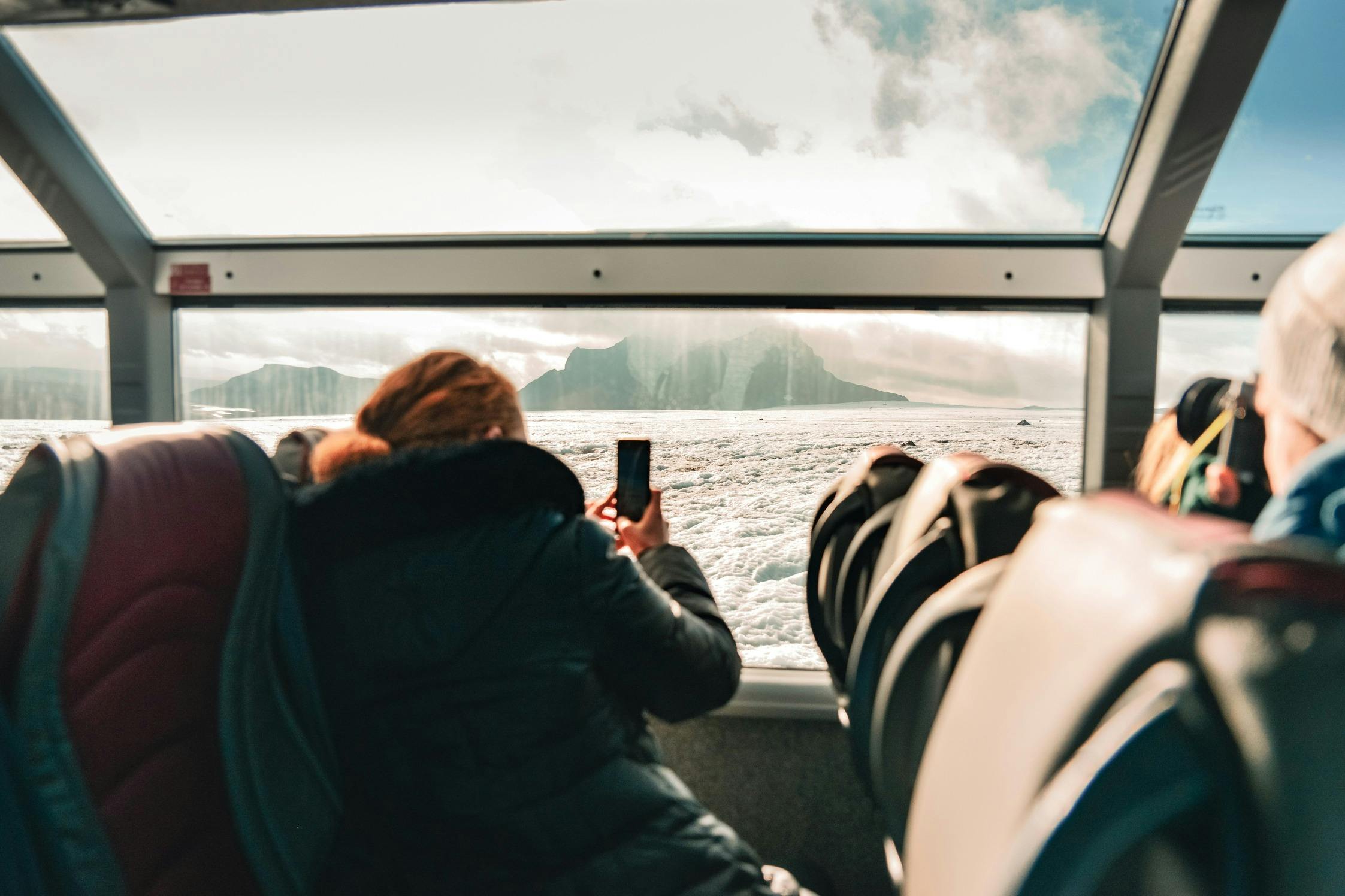 Persona che scatta una foto con un telefono dall&#39;interno di un veicolo simile a un autobus con grandi finestre, che si affaccia su un paesaggio innevato e sulle montagne.