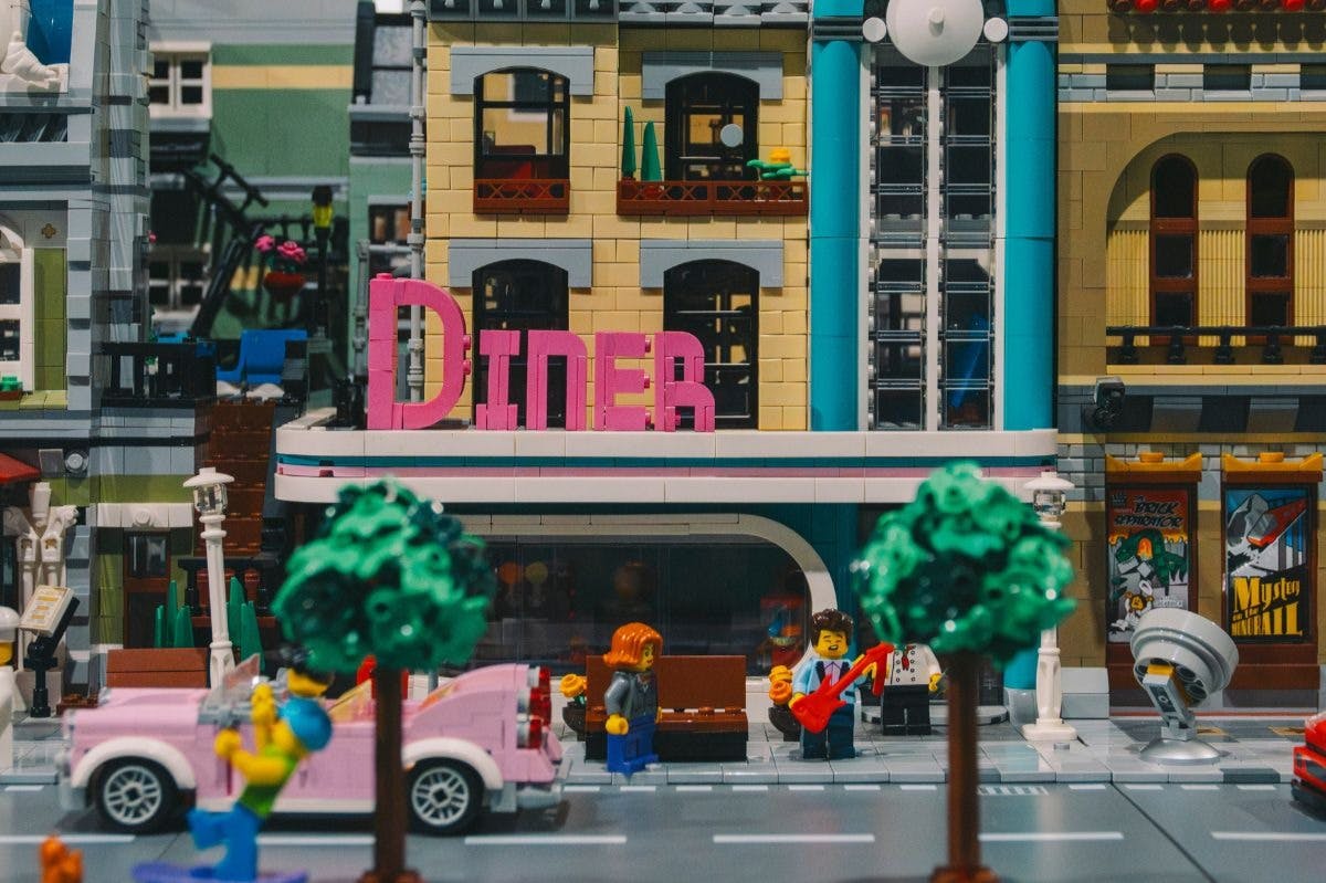 Une scène de restaurant LEGO avec une enseigne rose, des arbres, une voiture rose et des figurines, dont une jouant de la guitare rouge.