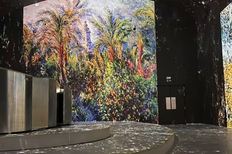 Une grande peinture murale d'intérieur représente un jardin vibrant avec des palmiers et des fleurs luxuriantes. Des structures métalliques réfléchissantes se trouvent sur la gauche.