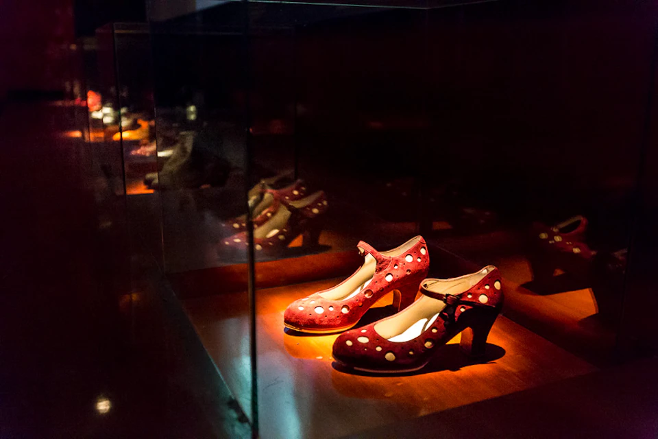 Red polka dot high-heeled shoes displayed in a dimly lit glass case, reflecting multiple times in the glass.