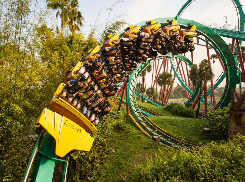 People riding a yellow rollercoaster upside down on a loop amidst lush greenery and palm trees.