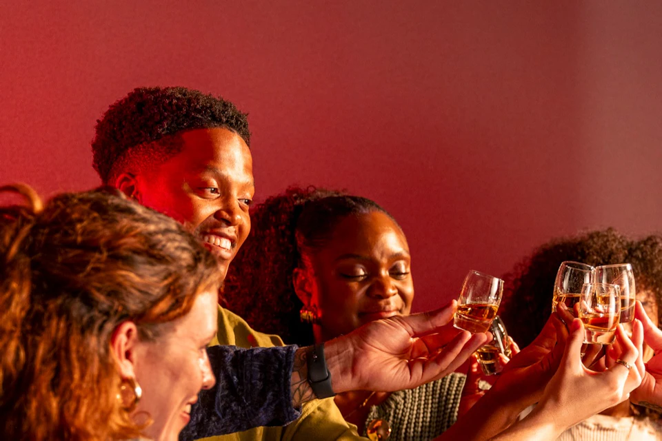 A group of people toasting with glasses around a table in a warmly lit setting, smiling and enjoying each other's company.
