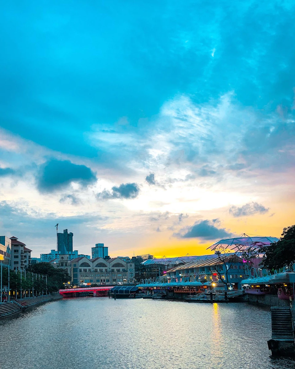 A riverside scene at sunset with buildings, bright umbrellas, and a blue sky with scattered clouds.