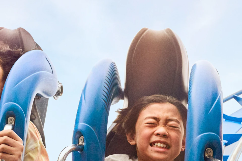 Three people seated on a roller coaster ride, holding handles, and expressing excitement and thrill.
