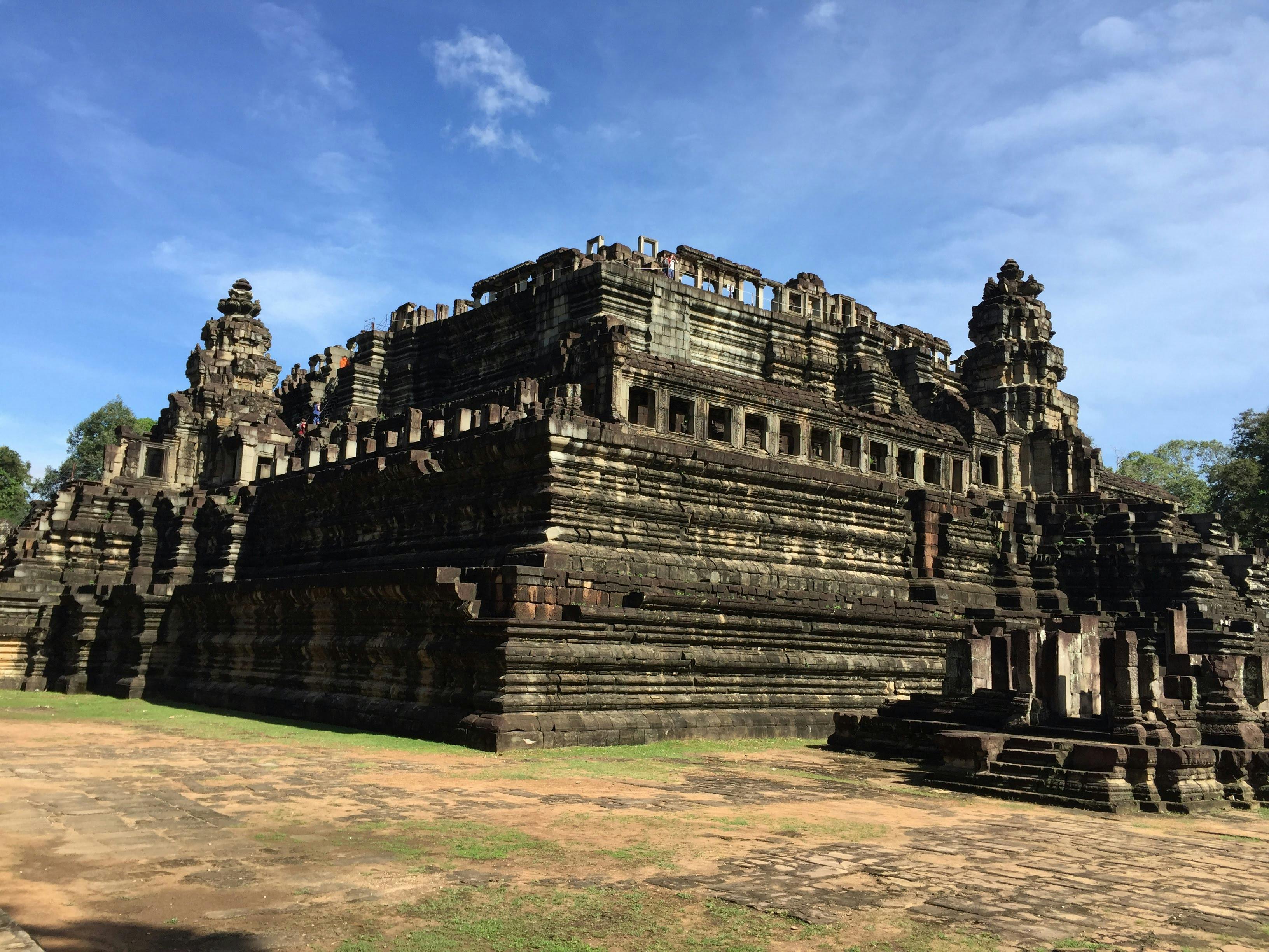 Ancient stone temple with intricate carvings, multiple levels, and towers, set against a blue sky with scattered clouds.