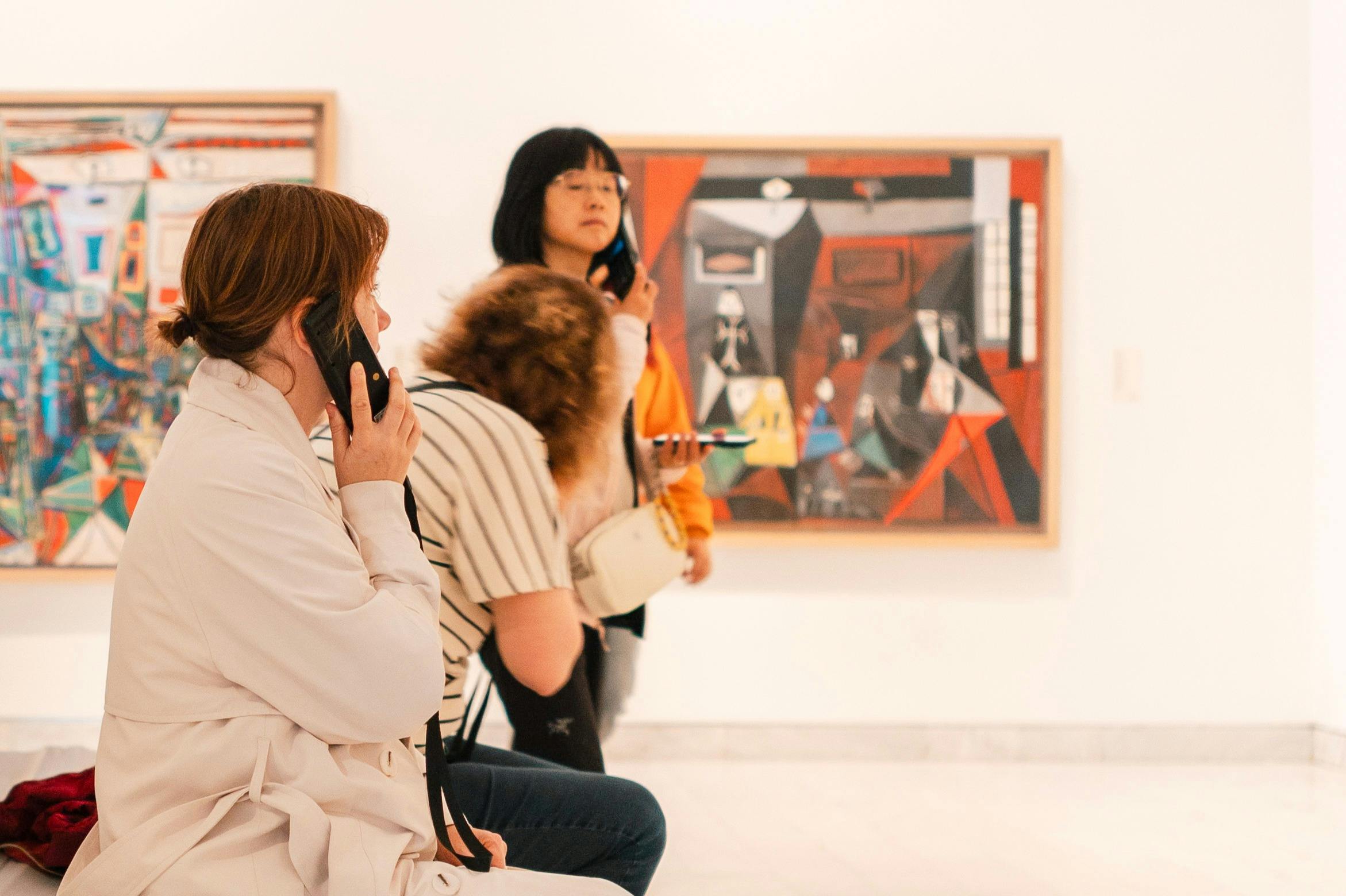 Visitantes en una galería de arte contemplando pinturas abstractas en las paredes, algunos utilizando audioguías.