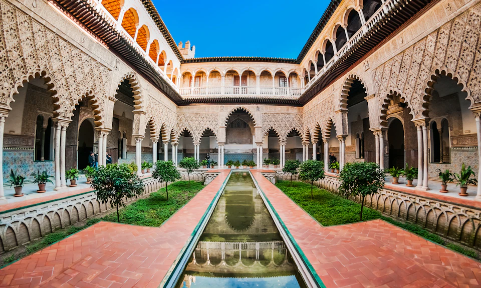 A courtyard with arched walkways, a central reflecting pool, and manicured greenery, surrounded by intricate architectural details.