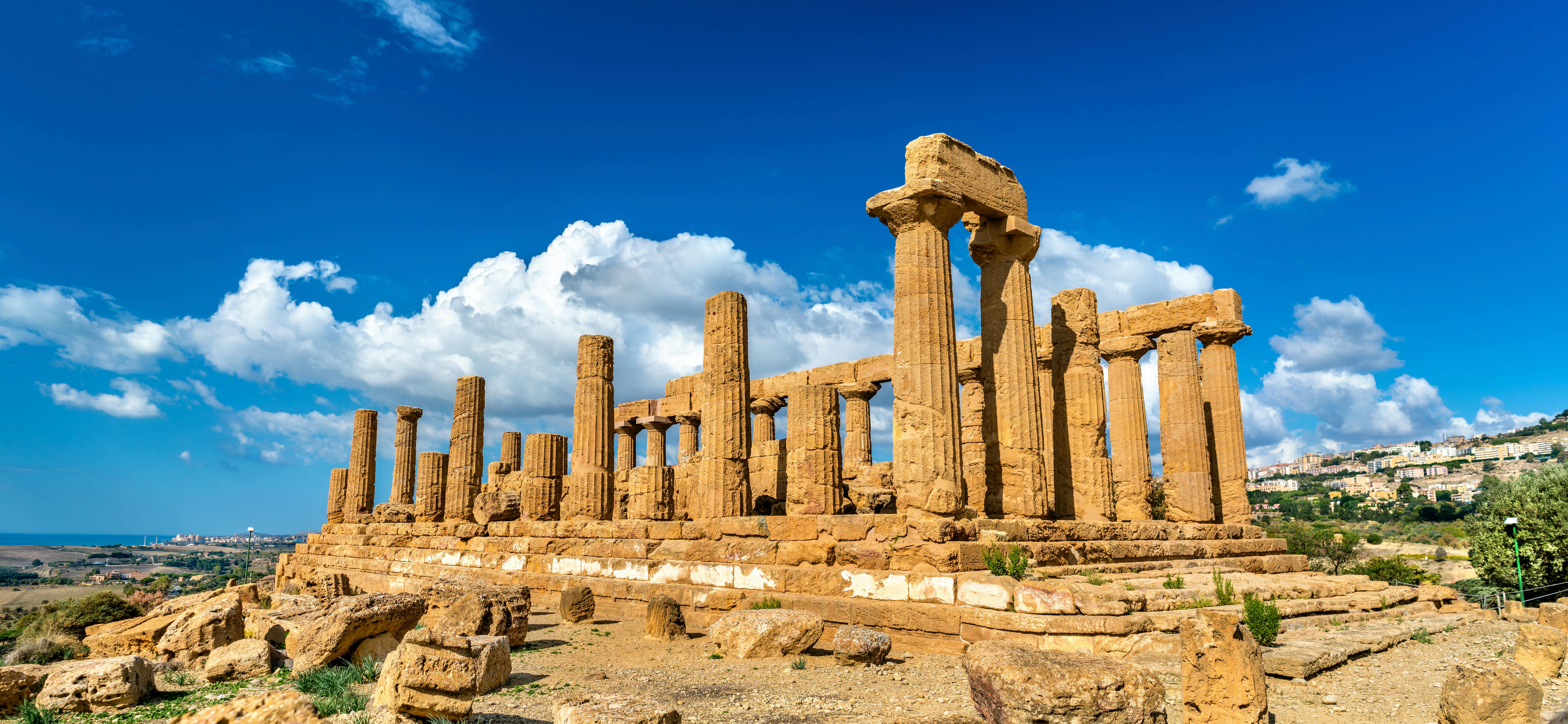 Ancient stone ruins with columns under a bright blue sky with white clouds.