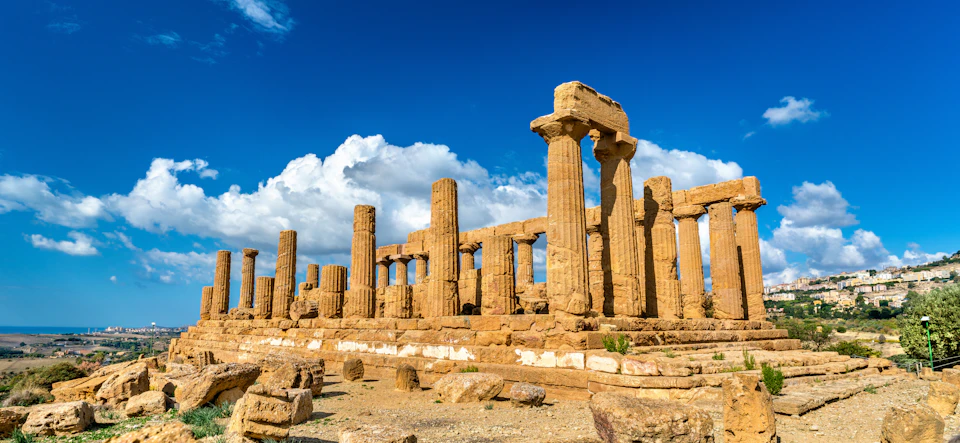 Ancient stone ruins with columns under a bright blue sky with white clouds.