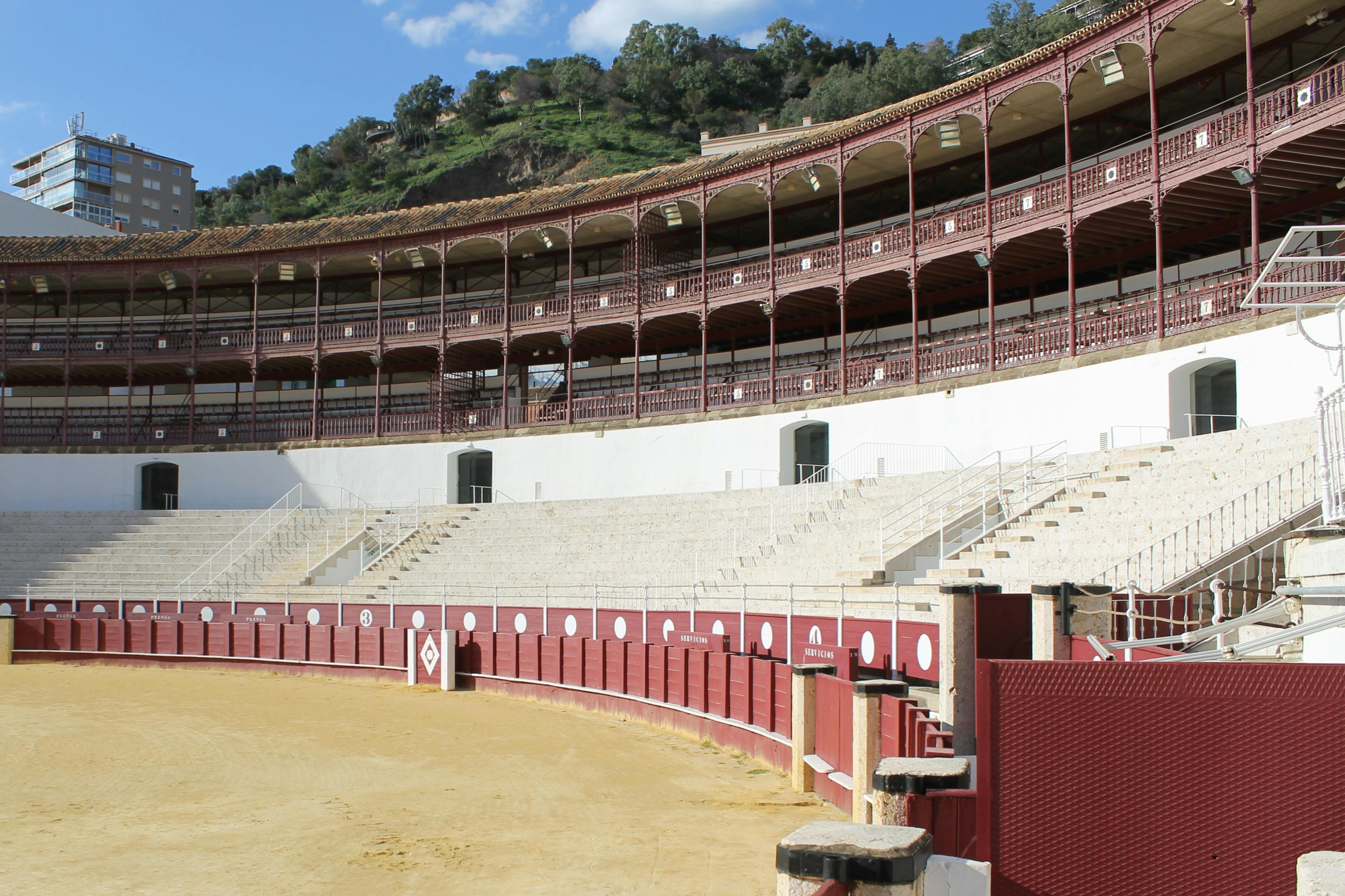 空荡荡的斗牛场，配有红色和白色路障、石头座椅和拱形盖板，矗立在绿色山坡的背景下。
