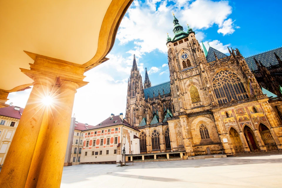 A Gothic-style cathedral with intricate spires and stained glass windows under a bright blue sky with scattered clouds.