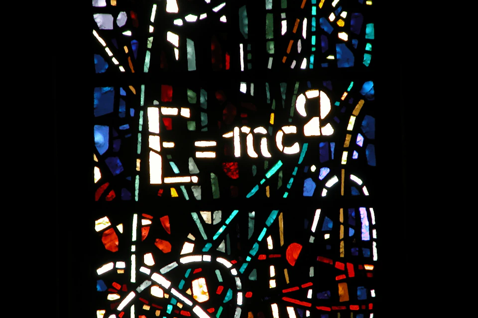 A stained glass artwork featuring the equation E=mc² prominently, surrounded by colorful abstract patterns.