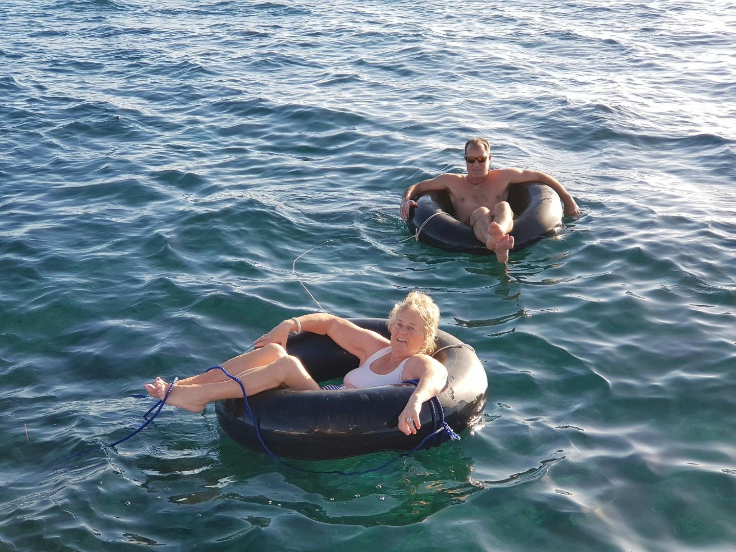 Two people relaxing on inflatable tubes floating on calm water under sunlight.
