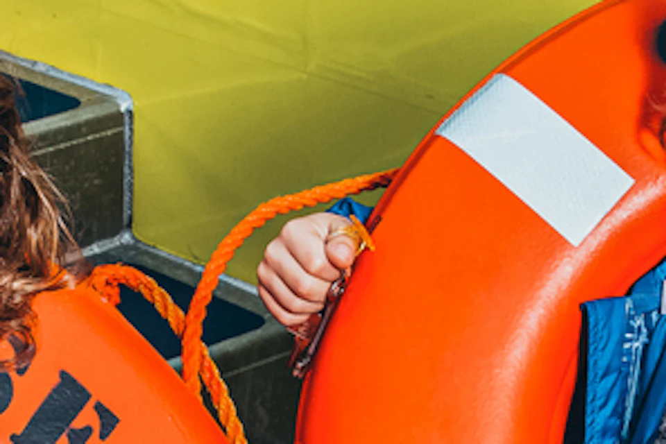 Two children standing on a boat deck, holding bright orange lifebuoys with "SEA DREAM" written on them, smiling at the camera.