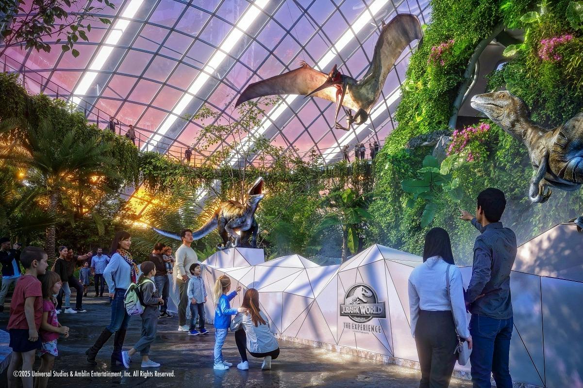 People exploring a Jurassic World-themed exhibit with dinosaur statues and a large pterosaur model in a glass-domed space.